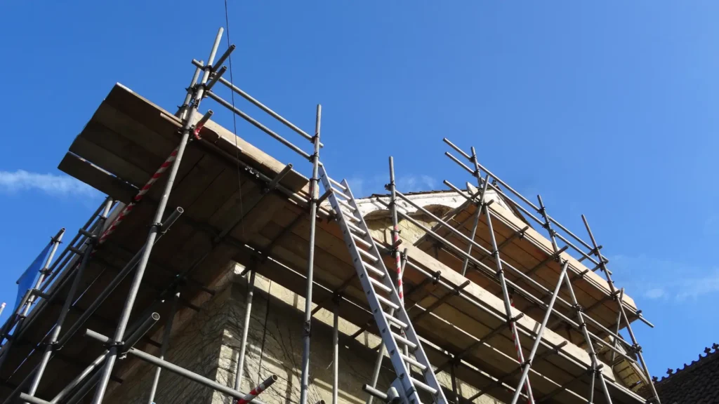 Rusztowania, pomosty, drabiny – jak wybrać odpowiednie zabezpieczenia podczas pracy na dachu - zdjęcie przedstawia rusztowania i drabinę prowadzącą na remontowany dach